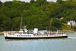 Broadside view of ship, with black hull and white superstructure, steaming right to left