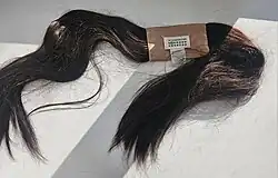 Dark brown hair scarf laid flat on white surface with sewn fabric label at center connecting two tapered ends