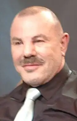 Slightly blurred portrait style Image of Therry Mugler wearing a silver dress tie and black or dark brown dress shirt in warm lighting
