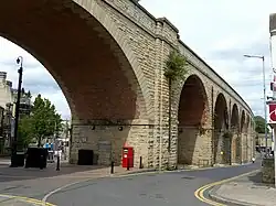 High elevated multiple arched structure in natural stone with red brick under arches stretching across town centre supporting rail tracks in either direction towards town of Worksop and city of Nottingham