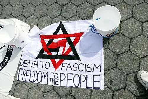 banner shows a Star of David made from a red triangle pointing down and a black triangle pointing up, the antifascist red and black flags a are in the center, and text under it says "death to fascism, freedom to the people"