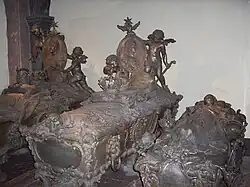 Three grey, ornamental sarcophagi standing next to each other, with a fourth underneath the one in the centre