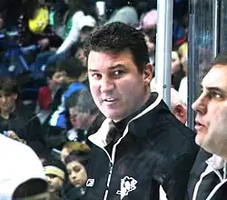 Middle-aged man with dark hair wearing a black sport jacket with a Pittsburgh Penguins logo