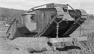 Black-and-white photo of a Mark IV tank climbing a rise, with a wooden beam suspended from chains at its front