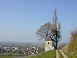An old stone watch tower stands at a mountain top road; past the road, layers of rounded hilltops illustrate the kind of terrain the combatants faced. In the distance a silvery shimmer on the horizon marks the location of the Rhine river.