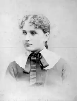 A young white woman with curly hair, wearing a white collar with a dark bow