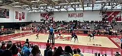 A volleyball match between two teams on a volleyball court surrounded by spectators.