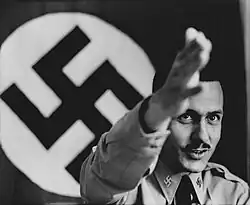 Koehl giving a sieg heil salute with a swastika behind him