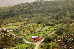 A photograph taken from a height shows a rural area with small fields and houses connected by dirt roads