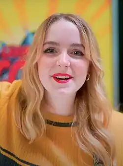 Mckenna Grace smiling against a yellow background at the 2023 German Comic Con
