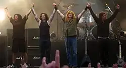 A four-piece band cheering the audience at the end of a concert