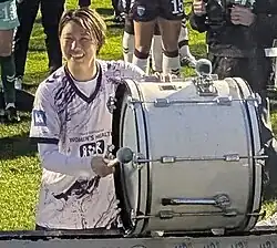 Player in uniform smiling and hitting a bass drum after a match