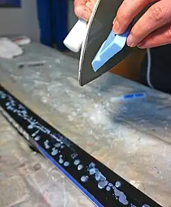 Melting glide wax onto a skate ski to be ironed in and scraped smooth