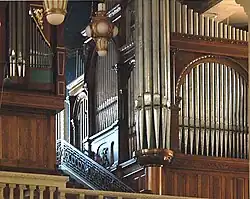 The metal pipes of two organs are in wooden cases of different dates and styles in the organ loft. To the side of the organ is a mosaic showing God as creator.