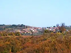Distant shot of a village framed by foliage of shrubs and trees, tinted with red and yellow. (Ikizce)