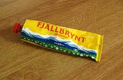 A yellow tube of primost with mountains and a field drawn on it.