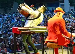 Musician Michael Guerra playing an accordion while facing an audience. To his right is keyboardist Jerry Dale McFadden, playing a piano keyboard while his back is to the camera