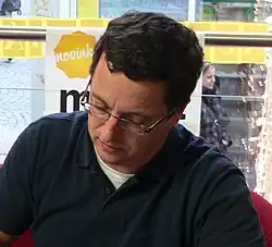 close-up of Michal Viewegh wearing a dark polo shirt over a white t-shirt, looking down, appearing to write