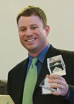 Mike Masnick holds a transparent glass award, smiling while posing for the camera.