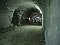 A long view down a lit gravel—paved concrete tunnel which has a series of openings on the left-hand side