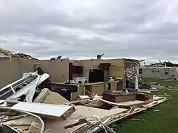 A yellow and damaged house with few walls and furniture standing