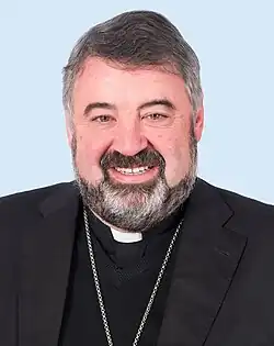 A smiling priest with a dark but greying beard