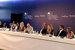 The cast and director sit at a long table