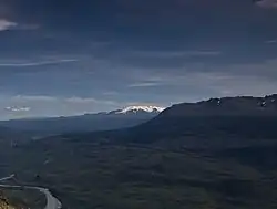A glaciated, flat-topped, gently-sloping mountain with a much lower barren mountain in the right foreground