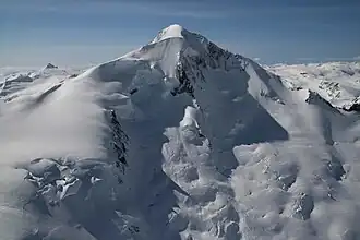 A snow-covered, symmetrical mountain with a sharp-pointed summit