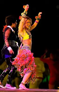 An image of a woman dancing is being projected onto a large screen. There is green lighting in the entire arena and large amounts of confetti are floating in the air.
