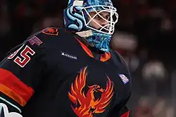 Ice hockey goaltender in a Coachella Valley Firebirds jersey in the goal crease with looking behind him