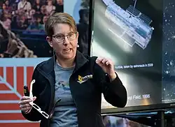 Jane Rigby speaks, wearing a JWST-themed jacket and a rainbow-flag-themed NASA t-shirt.