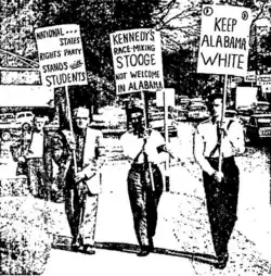 Three neo-Nazis marching down a sidewalk while holding signs