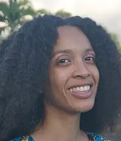 A portrait photograph of a smiling black woman with shoulder-length curly hair.