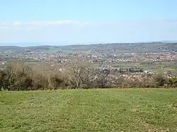 lots of house roofs, with trees and grass in the foreground and hills in the distance.