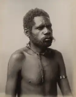 Portrait photograph of a shirtless Aboriginal man with a cord necklace and a band around his upper arm