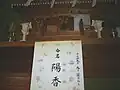 A wooden household shrine featuring two tōrō lanterns made of wood, and a piece of paper announcing the name of a baby.