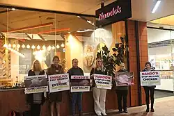 Six people holding placards calling for better chicken welfare outside a Nando's store in Wellington, New Zealand.