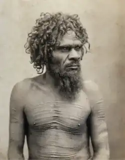 Portrait photograph of a shirtless Aboriginal man with a scarred torso