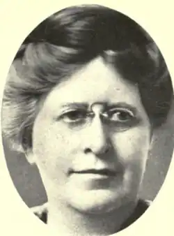 A white woman with hair in a bouffant updo, wearing glasses, in an oval frame