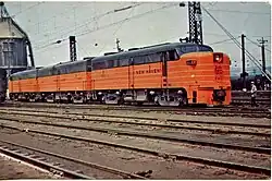 Three ALCO FA locomotives parked on a track in the yard. A railroad worker is standing near the lead locomotive.