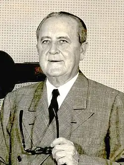 Niles Trammell, holding a pair of glasses in his left hand, standing next to a television camera with labels for "WCKT" and "RCA Television" on it