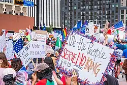 Protestors holding signs, the most prominent one reading "We the People Serve No King"