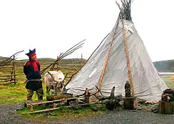 A Sámi settlement near the North Cape in Norway, showing a traditional tent, a person in Sámi clothing, and a reindeer in an outdoor setting.