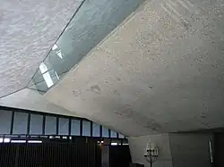 The bush-hammered concrete wall overhangs the hallway at right. The glass panels separate the overhanging walls from the ceiling and provide indirect natural light to the sanctuary.