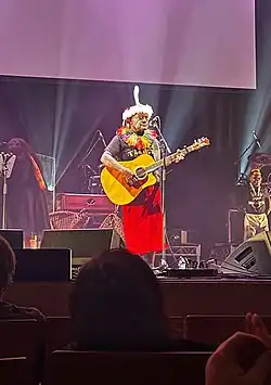George Telek performing on stage while playing an acoustic guitar