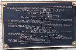 A commemorative plaque, mounted on the Burd Street side of the bank building located on South Broadway & Burd Street in Nyack. The inscription says "Nay-ACK, which being translated means THE FISHING PLACE...The First Settlement ...Rockland County, NY...took place in 1675."