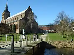 St. Canute's Cathedral seen from Eventyrhaven park. The statue represents Hans Christian Andersen. The yellow building stands on the site of the former St. Canute's Abbey