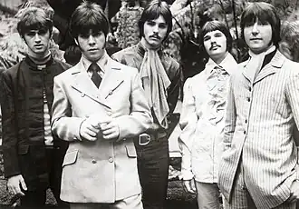 Black and white photo of five men in their late twenties with long hair.