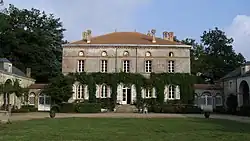 Facade of the château, consisting of a single main building covered with virgin ivy on the ground floor and opening onto a lawn courtyard
